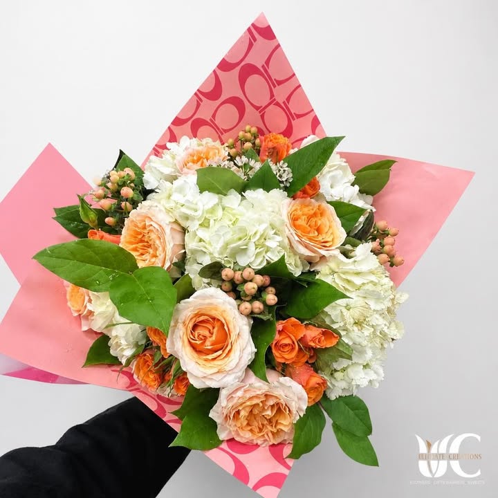 Lush peach and white bouquet wrapped in pink patterned paper with green foliage.