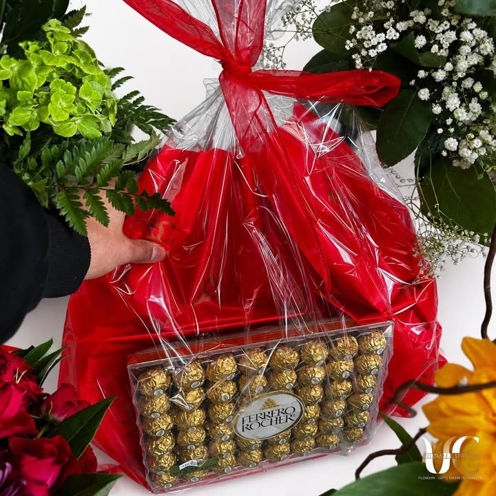 Red-wrapped chocolate gift surrounded by colorful flowers and greenery