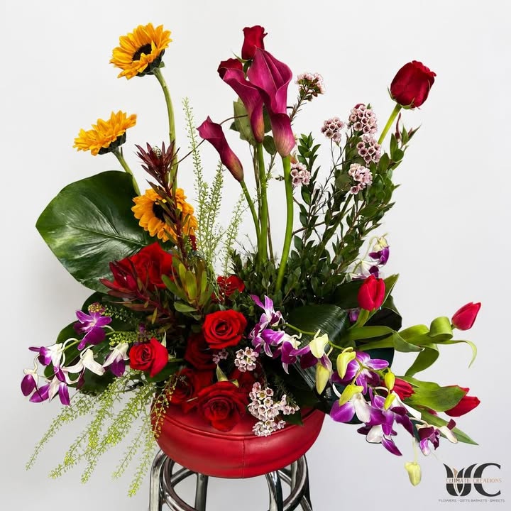 Lush red-vessel arrangement with roses, sunflowers, purple orchids, and greenery