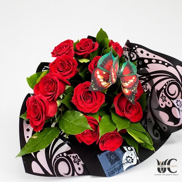 Red rose bouquet with green leaves, butterfly accent, and black-and-pink wrapping