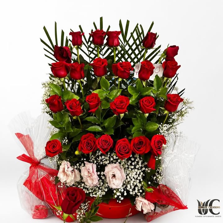 Tall layered floral display with red roses, greenery, white filler flowers, and pale pink blooms