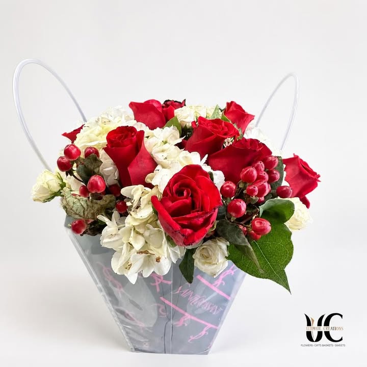 Clear handled flower box with red roses, white blooms, red berries, and green foliage.
