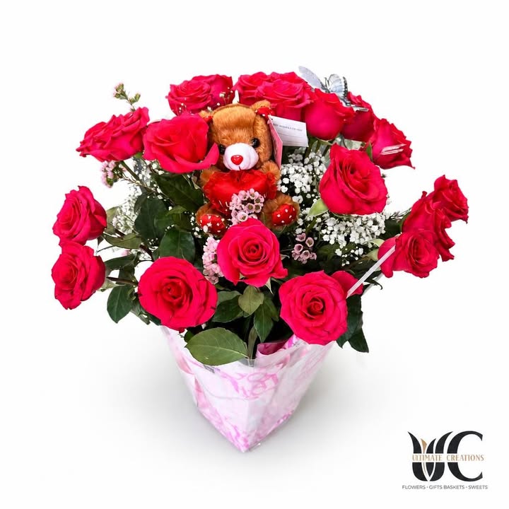 Bright pink and red rose bouquet with teddy bear, white filler flowers, greenery, and pink wrapping.