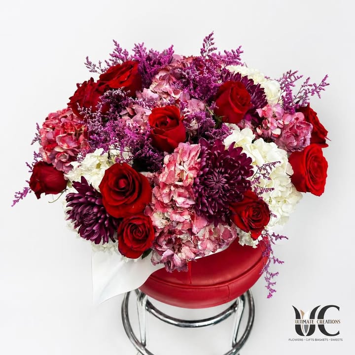 Lush red, pink, white, and purple flower arrangement in a round red box