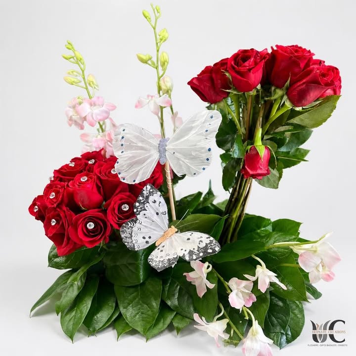 Red rose arrangement with pale pink blossoms, greenery, and white decorative butterflies.