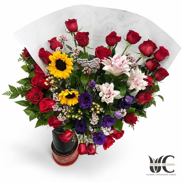 Colorful bouquet with red roses, yellow sunflowers, purple blooms, pink accents, greenery, and a Valentine’s Day pick