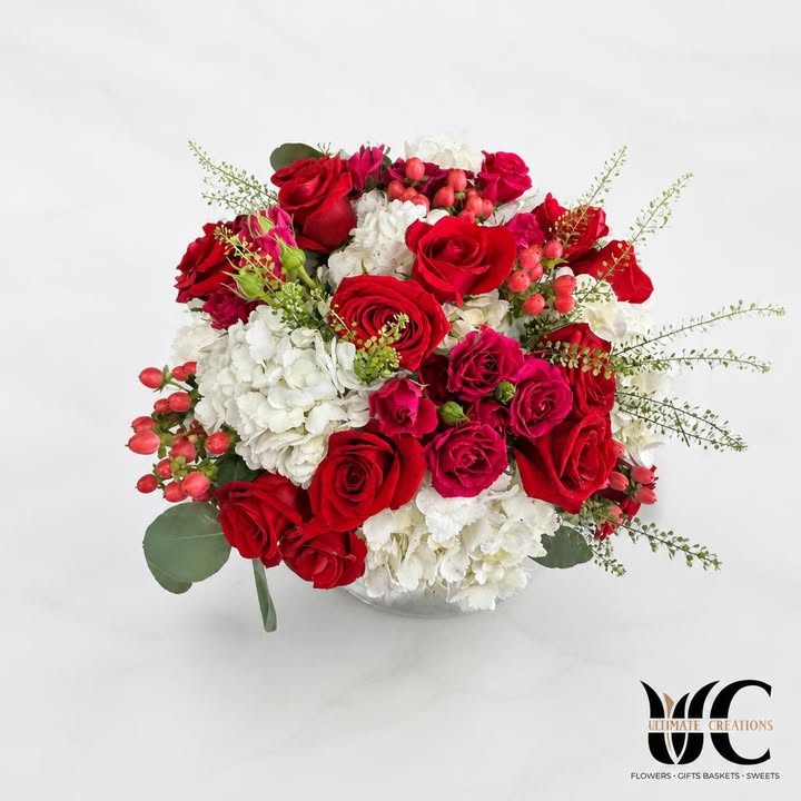 Lush red, white, and pink bouquet with green foliage against a leafy backdrop.