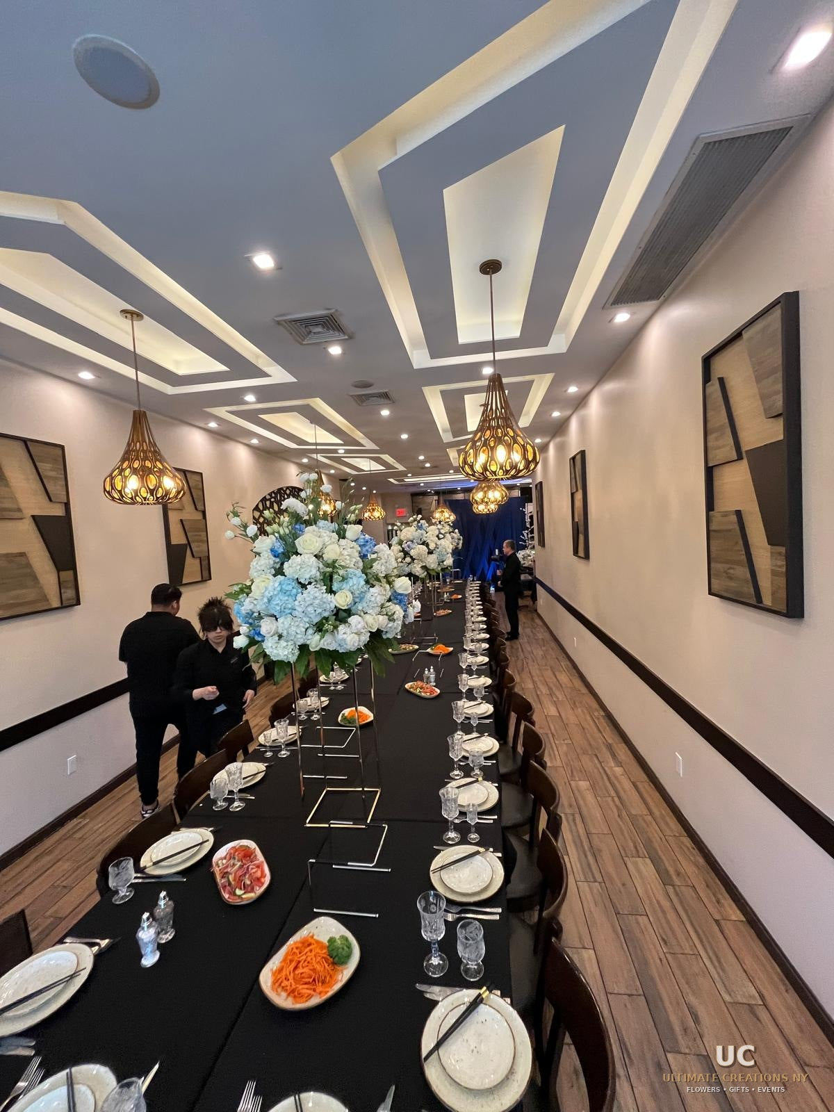 Full-room 50th birthday dinner setup with black tables, tall floral centerpieces, and navy backdrop by Ultimate Creations NY