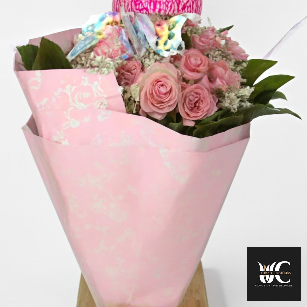 Pink rose bouquet wrapped in blush paper with green leaves and decorative accents.