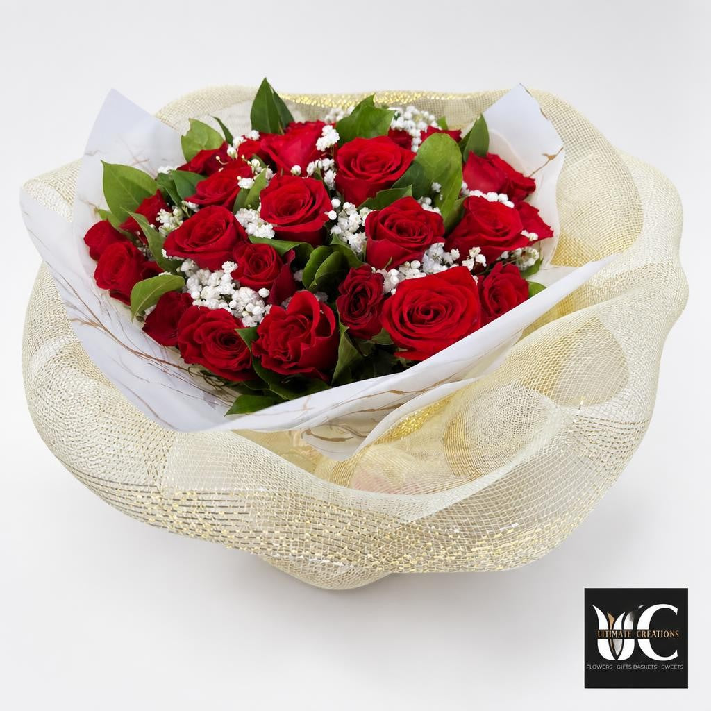 Full bouquet of crimson roses with white filler flowers and green foliage, surrounded by decorative white and metallic-textured wrapping.