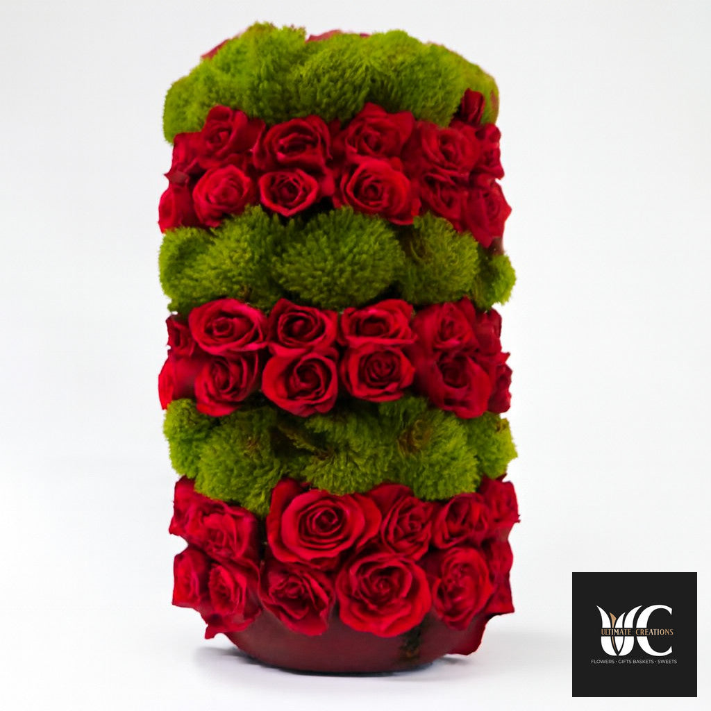 Tall vase arrangement with horizontal bands of red roses and green cushion flowers.