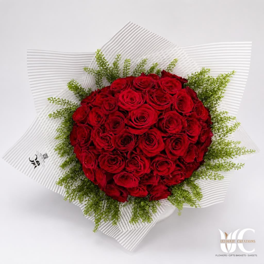 Round bouquet of tightly clustered deep red roses with fine green filler and black-and-white striped wrapping.