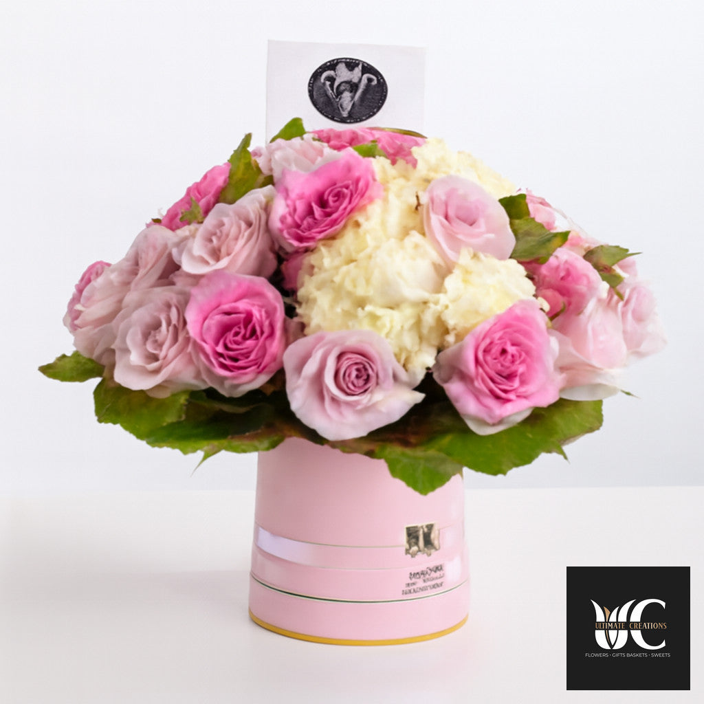 Pink and cream floral arrangement in a pale pink hat box with roses, hydrangea, and greenery.