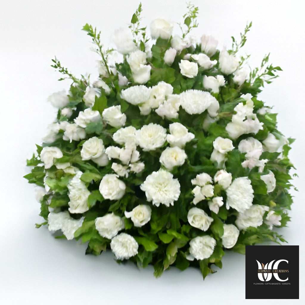 Large round white floral arrangement with mixed white blooms and green foliage on a white background.