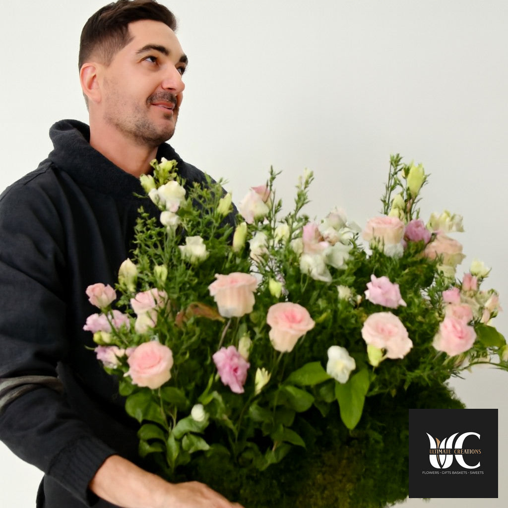 A man holding a large bouquet of pink and white flowers with lush greenery.