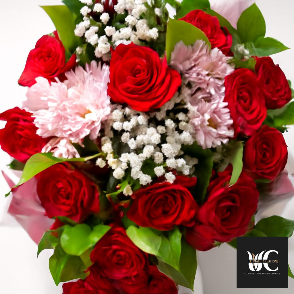 Bouquet of red roses with pink flowers, white filler blooms, and green leaves.