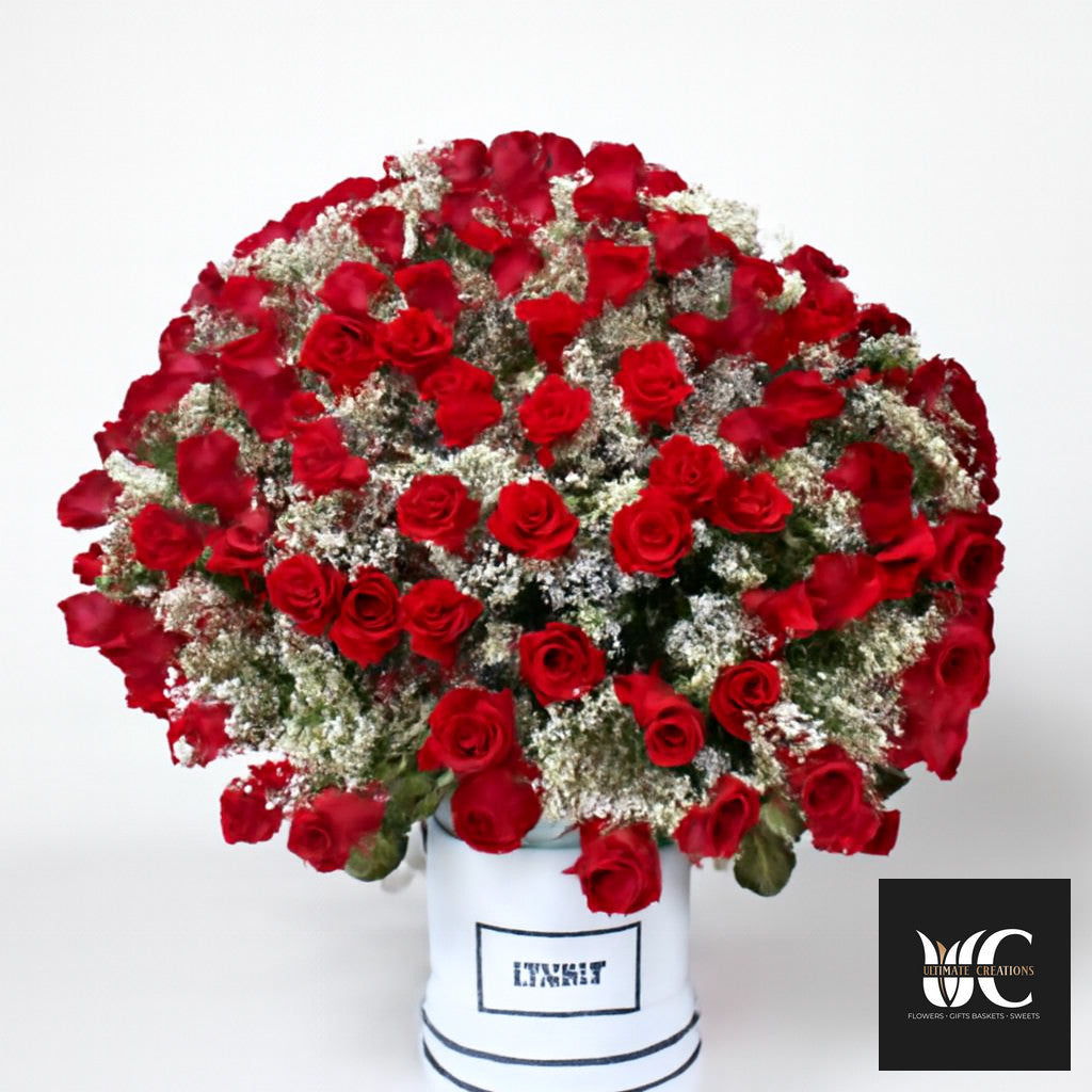 Large round arrangement of red roses and white filler flowers in a white cylindrical box.
