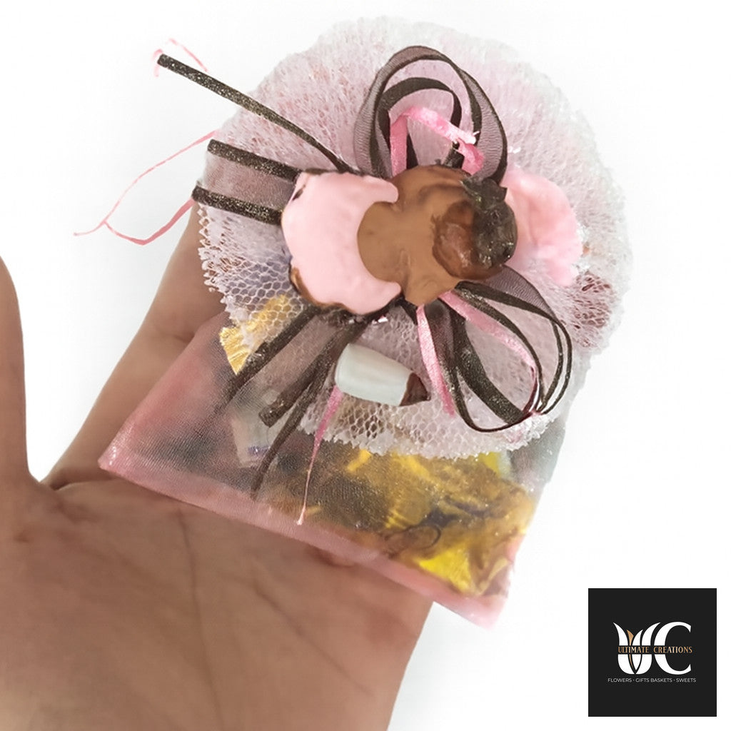Handmade pink and brown favor bag wrapped with tulle, ribbon, and small sweets held in a hand.