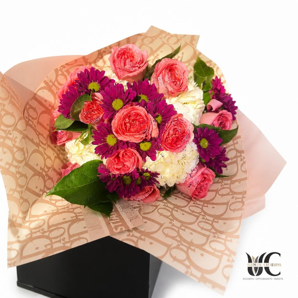 Wrapped bouquet with coral-pink roses, magenta daisy-like flowers, white hydrangea, green leaves, and patterned paper.