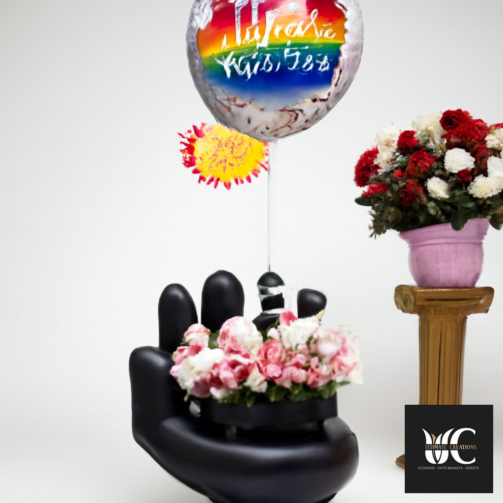 Rainbow balloon above pink and white flowers arranged on a black sculptural base, with a separate red and white flower arrangement on a pedestal.