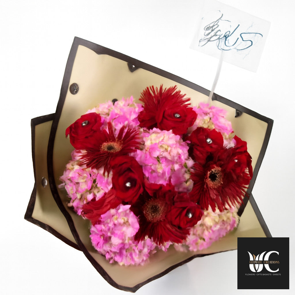 Hand-tied bouquet with red and pink flowers wrapped in cream and black paper.