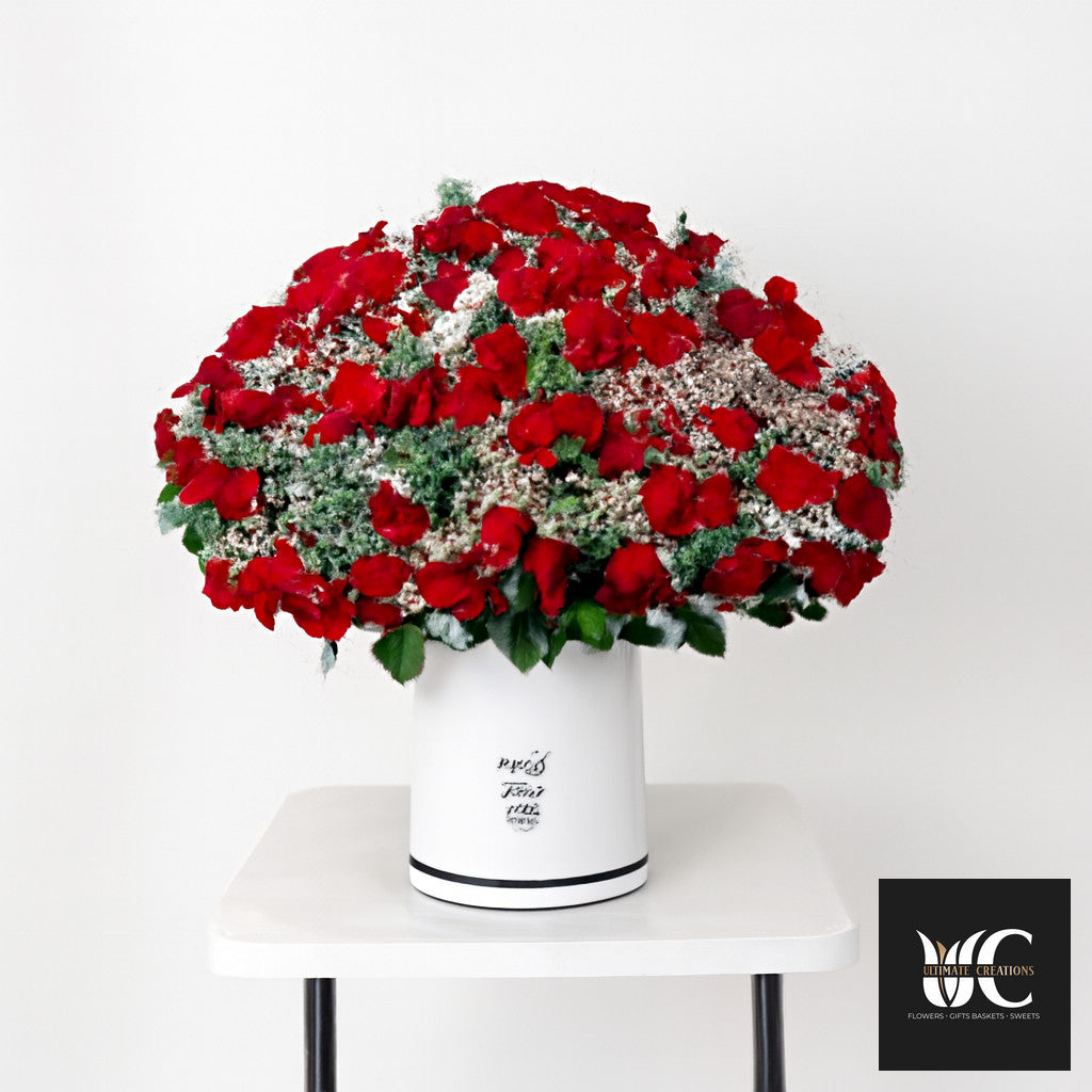 Large dome-shaped red flower arrangement with white filler and greenery in a white cylinder vase.