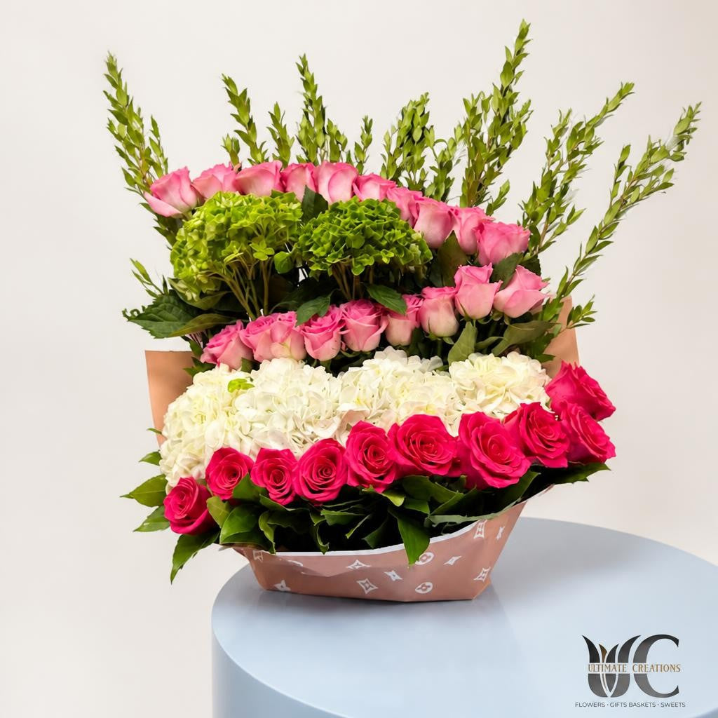 Structured flower box with rows of pink roses, white hydrangea, green blooms, and tall greenery in warm-toned wrapping.