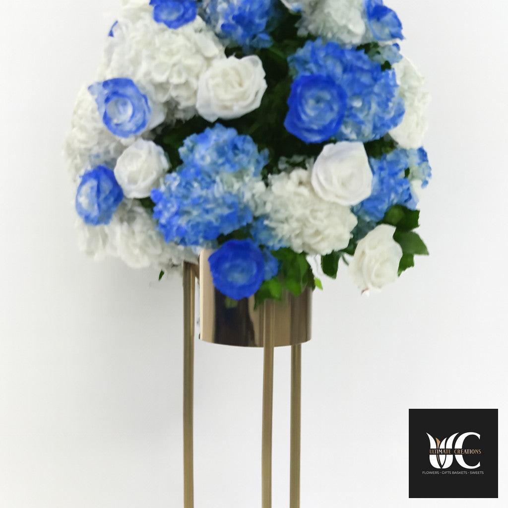 Blue and white floral arrangement on a tall gold pedestal stand.