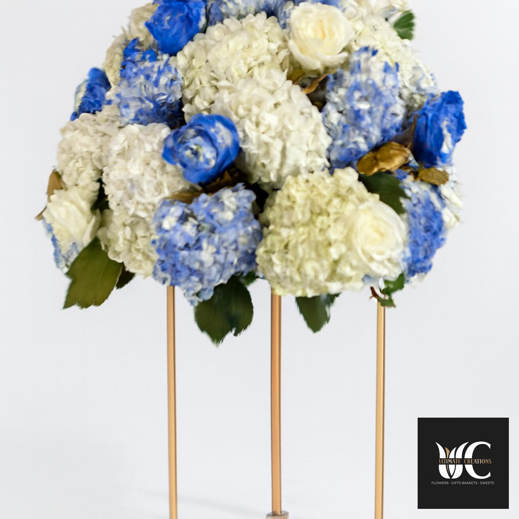 Blue and white floral centerpiece arranged on a tall gold stand.