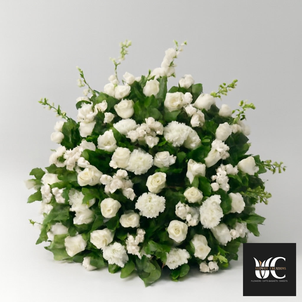 Large white floral standing arrangement with mixed blooms and green foliage against a plain background.