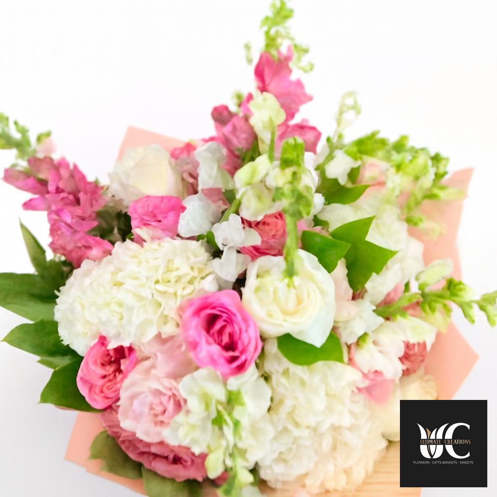 A lush bouquet of pink, white, and green flowers wrapped in pale peach paper.