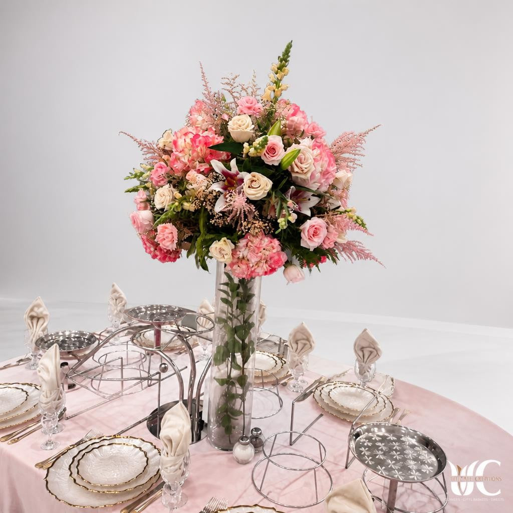 Tall blush and cream floral centerpiece in a clear glass vase on a formal pink table setting