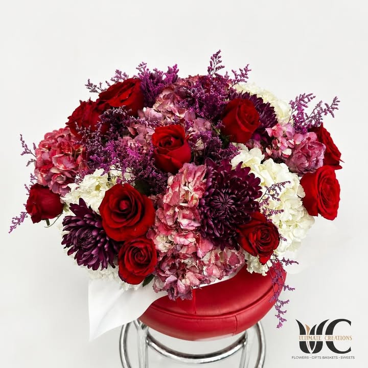 Lush red, pink, purple, and white flower arrangement in a red round box