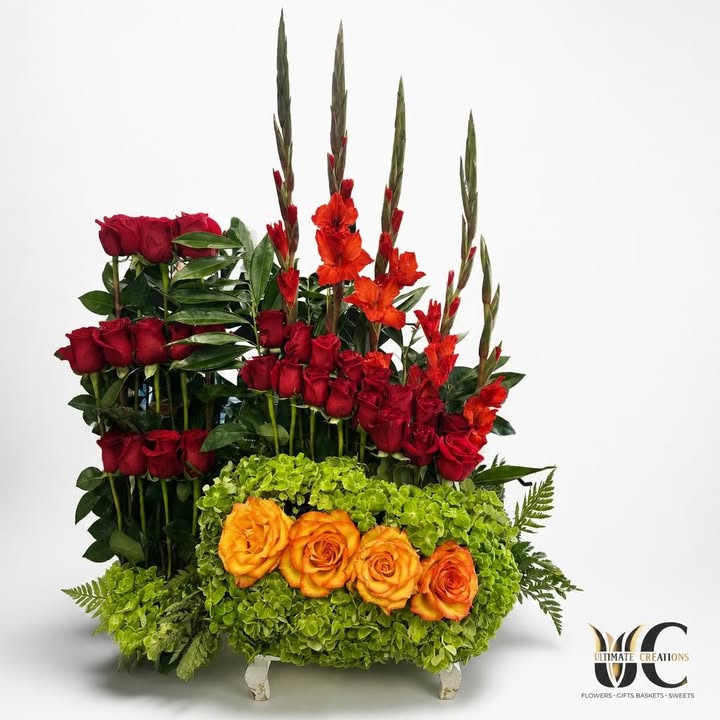 Layered floral arrangement with red roses, red-orange blooms, orange roses, green flowers, and foliage