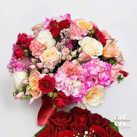 Full mixed bouquet of red, pink, peach, cream, and white flowers with coordinating wrap