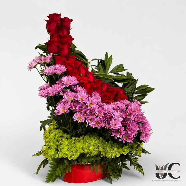 Colorful floral centerpiece with red roses, pink blooms, lime-green flowers, and greenery in a red container.
