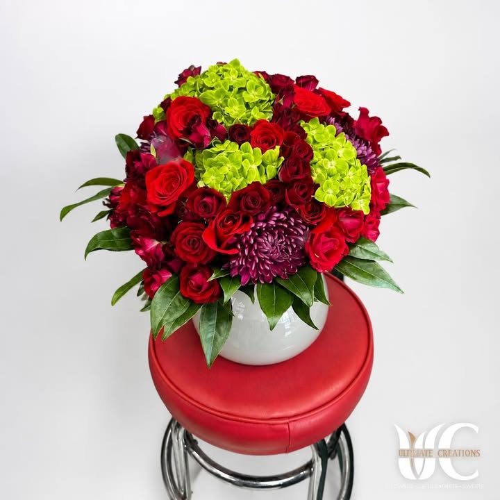 Round red, lime-green, and purple floral arrangement in a white vase.