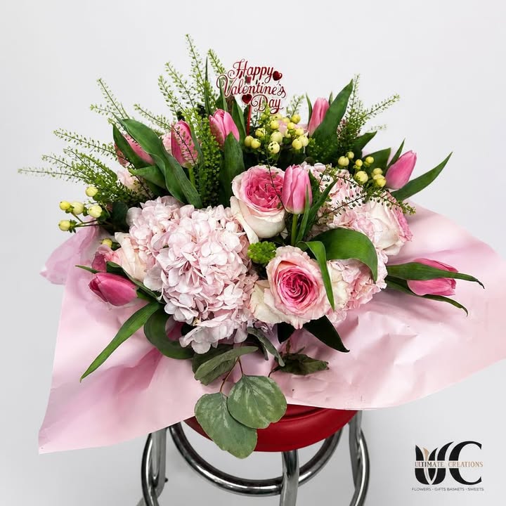 Wrapped pink bouquet with roses, tulips, hydrangea, yellow berries, and greenery.
