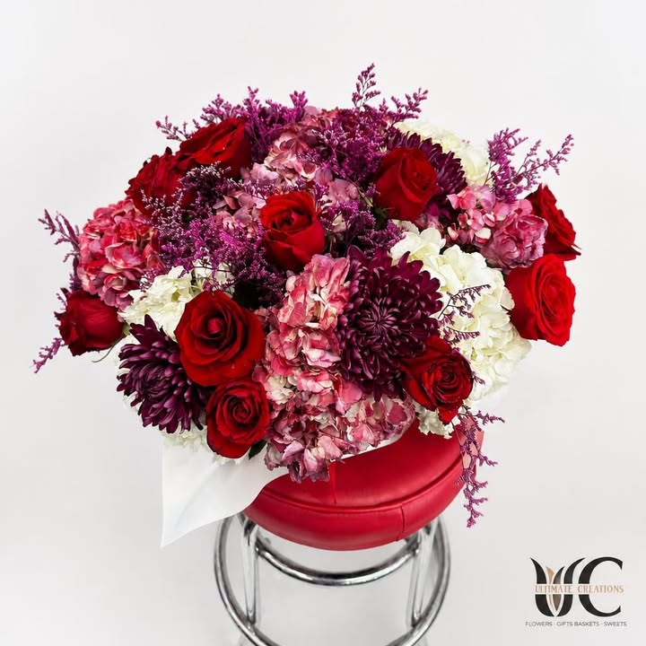 Lush bouquet of red roses, pink and white blooms, purple flowers, and greenery wrapped in white paper