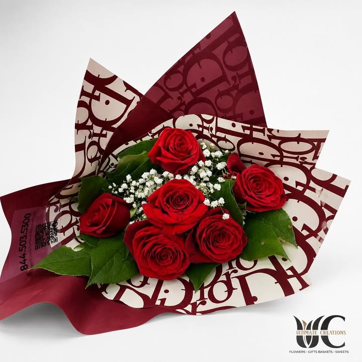 Bouquet of red roses with white filler flowers and green leaves in patterned burgundy wrapping