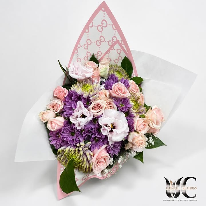 Lush bouquet of pink roses, purple blooms, white accents, and greenery in pink patterned wrapping