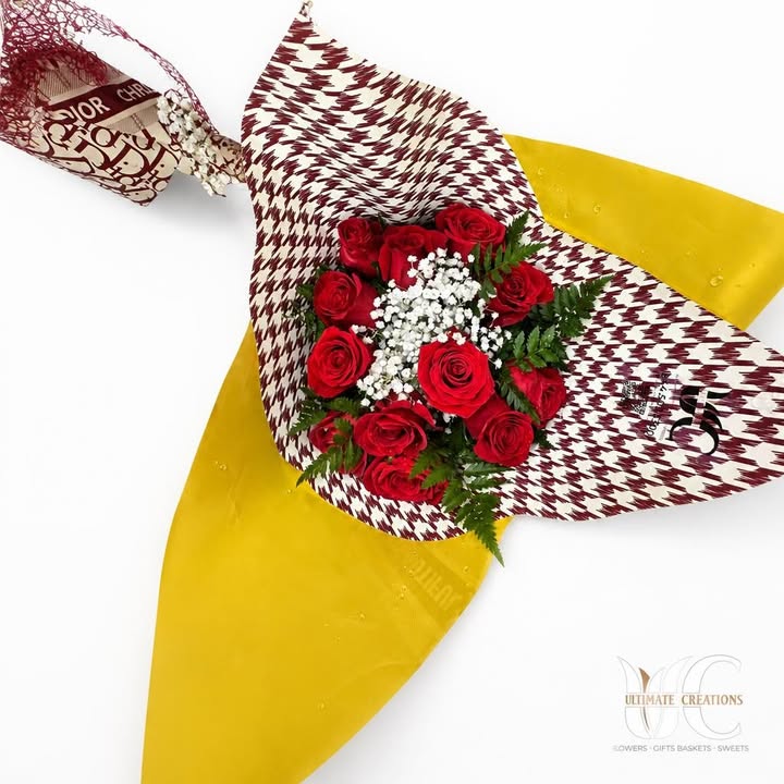 Wrapped bouquet of red roses with white filler flowers, fern greenery, and bold patterned paper