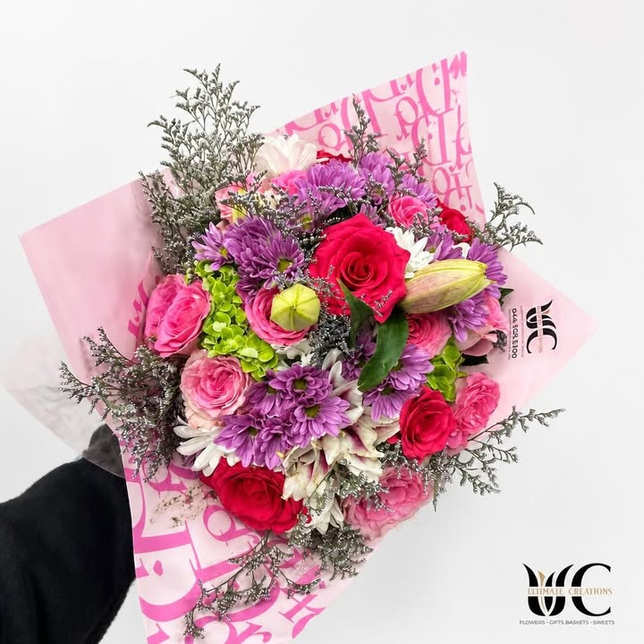 Mixed pink, purple, white, and red flower bouquet in pink wrapping.