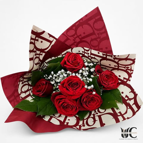 Bouquet of red roses with white filler flowers, greenery, and patterned red-and-white wrapping