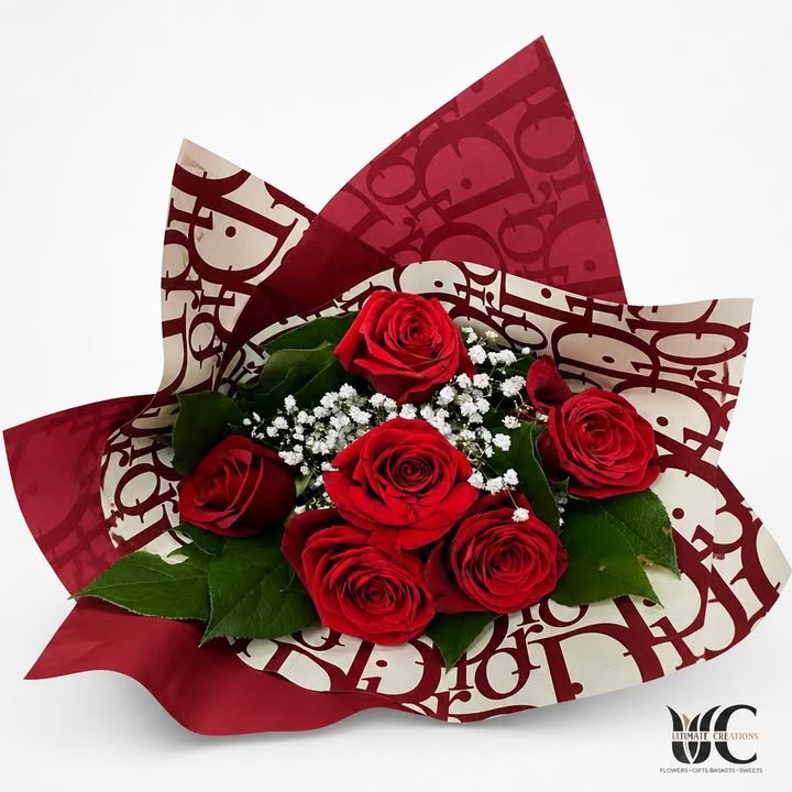 Bouquet of red roses with white filler flowers, greenery, and patterned red-and-white wrapping