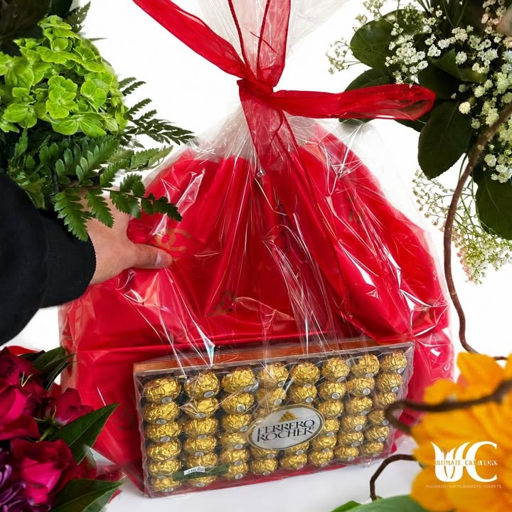 Red-wrapped floral gift presentation with gold-wrapped chocolates, greenery, and colorful flowers.