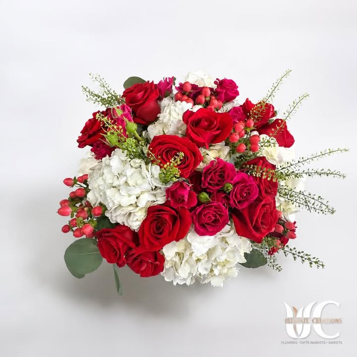 Lush bouquet of red and pink blooms with white flowers, berries, and greenery.