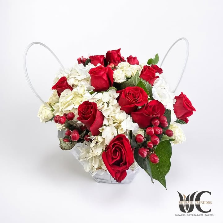 Red and white rose arrangement with greenery in a white handled container