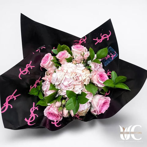 Pink and white flower bouquet with greenery in black wrapping with pink accents.