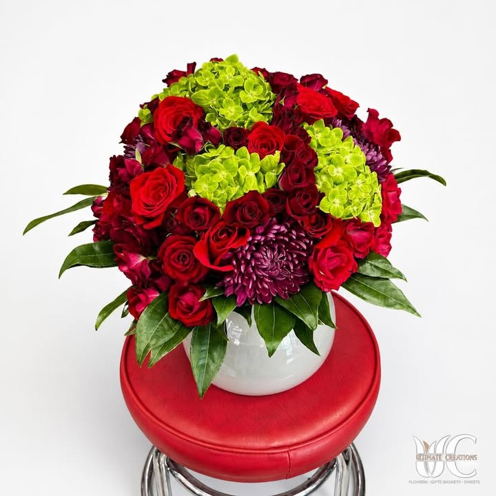 Lush red and burgundy flower arrangement with green blooms and purple accent in a white vase